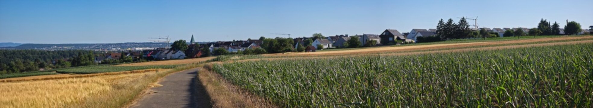 germany, magnificent wide panoramic country road approaching ostfildern kemnat through flourishing rural fields beneath radiant summer blue sky