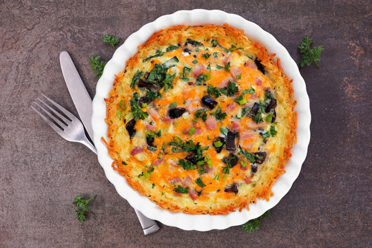 Breakfast quiche with ham, mushrooms, and onions made in a hash brown shell. Above view table scene on a dark background.