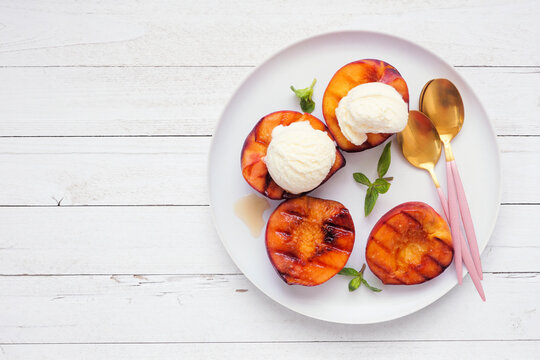 Sweet grilled peaches with vanilla ice cream. Overhead view on a white wood table background.