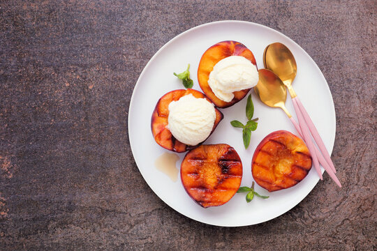 Sweet grilled peaches with vanilla ice cream. Top down view on a dark background.