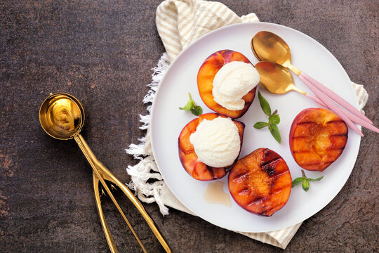 Sweet grilled peaches with vanilla ice cream. Top view table scene on a dark background.