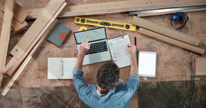 Carpenter, man and writing with laptop in warehouse above for timber production or distribution. Top view, male person or carpentry designer with computer or documents for lumber project or planning