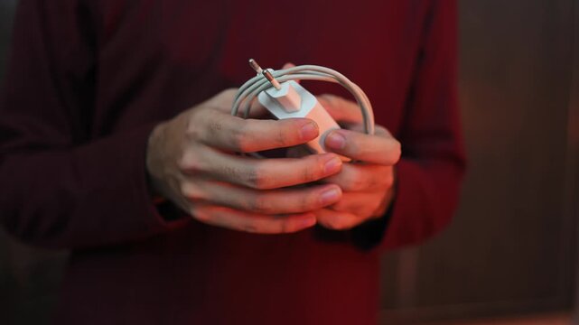 Phone charger. Cable for phone. Fast charging. A man winds up a long white cable to charge the battery on his phone