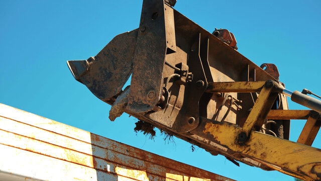 Front loader bucket containing dirt and debris, dumping material into the back of a large truck under a clear blue sky, highlighting industrial work in progress