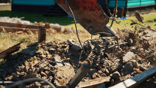 Excavator attachment breaking up a reinforced concrete foundation, creating a pile of rubble and rebar during construction site clearing and demolition activity
