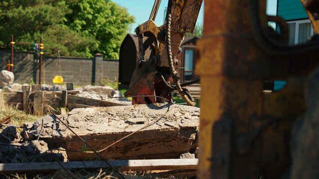 Heavy machinery excavator breaking up a large concrete slab with its bucket attachment, creating debris and rubble on a demolition construction site
