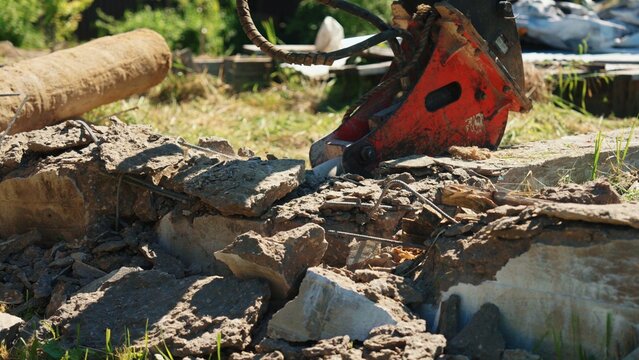 Hydraulic breaker attachment on an excavator arm performing demolition work, breaking apart reinforced concrete debris with exposed rebar at a construction site