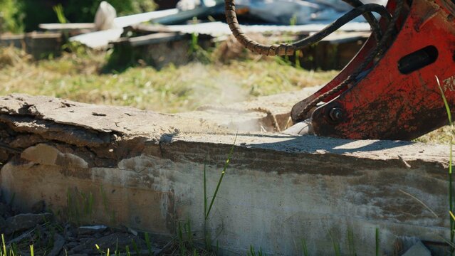 Close-up of a hydraulic breaker chiseling a reinforced concrete foundation wall with visible dust during residential demolition, showing structural removal, heavy equipment and site preparation.