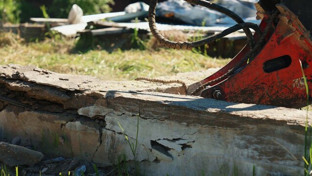 Hydraulic breaker attachment from heavy equipment demolishing a concrete wall, showing debris and dust in a construction site for renovation