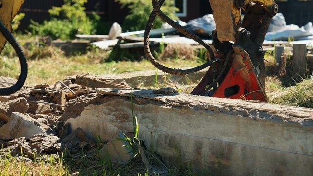 Excavator machine with a hydraulic attachment breaking apart a reinforced concrete foundation, creating debris and rubble during a demolition or renovation project
