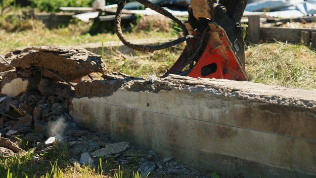 Close-up of a hydraulic breaker demolishing a reinforced concrete foundation wall with cracked concrete, exposed reinforcing steel and dust during residential site demolition and structural removal.