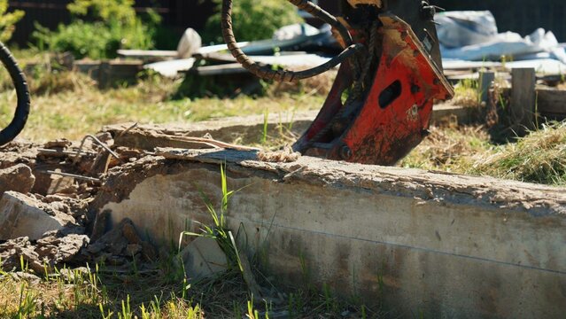 Close-up of a hydraulic breaker resting behind a cracked reinforced concrete foundation wall during residential demolition, showing heavy equipment, structural removal and site preparation.