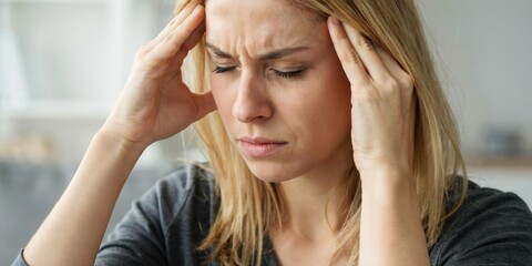 Fototapeta premium Young woman with blonde hair holding her temples and closing her eyes in pain.