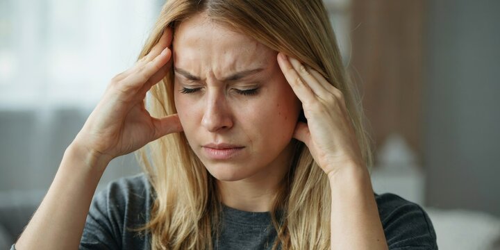 Close up of woman's face holding head in hands with pain.