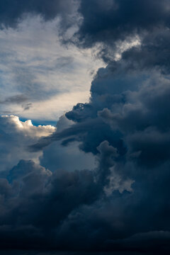 Dramatic dark storm clouds in deep blue sky. Vertical view of heavy dark storm clouds accumulating in blue sky, creating dramatic and powerful weather backdrop