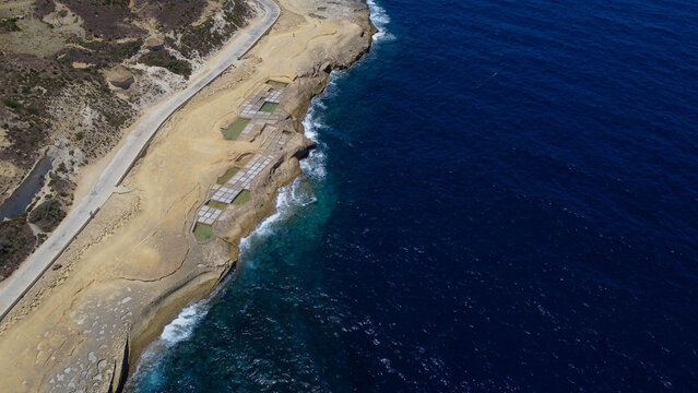 Xwejni s centuries-old salt pans unfold along the rugged coast of Zebbug, Gozo, geometric pools and vivid Mediterranean blues in a sweeping summer Aerial view