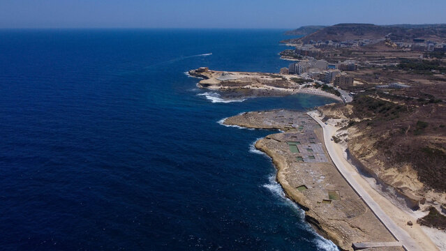 Xwejni s centuries-old salt pans unfold along the rugged coast of Zebbug, Gozo, geometric pools and vivid Mediterranean blues in a sweeping summer Aerial view