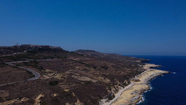 Xwejni s centuries-old salt pans unfold along the rugged coast of Zebbug, Gozo, geometric pools and vivid Mediterranean blues in a sweeping summer Aerial view