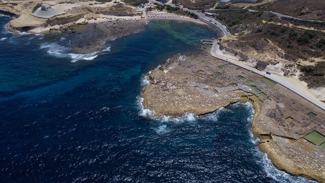 Xwejni s centuries-old salt pans unfold along the rugged coast of Zebbug, Gozo, geometric pools and vivid Mediterranean blues in a sweeping summer Aerial view