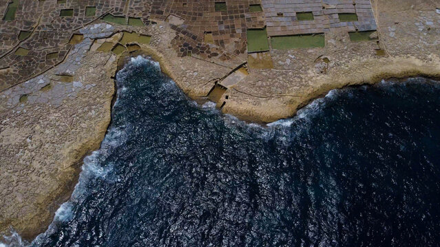 Xwejni s centuries-old salt pans unfold along the rugged coast of Zebbug, Gozo, geometric pools and vivid Mediterranean blues in a sweeping summer Aerial view