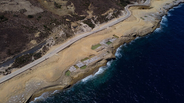 Xwejni s centuries-old salt pans unfold along the rugged coast of Zebbug, Gozo, geometric pools and vivid Mediterranean blues in a sweeping summer Aerial view