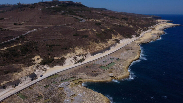 Xwejni s centuries-old salt pans unfold along the rugged coast of Zebbug, Gozo, geometric pools and vivid Mediterranean blues in a sweeping summer Aerial view