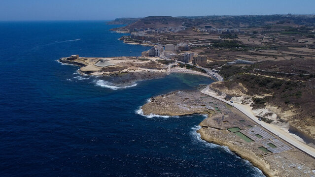 Xwejni s centuries-old salt pans unfold along the rugged coast of Zebbug, Gozo, geometric pools and vivid Mediterranean blues in a sweeping summer Aerial view