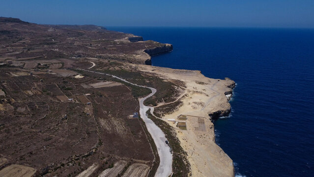 Xwejni s centuries-old salt pans unfold along the rugged coast of Zebbug, Gozo, geometric pools and vivid Mediterranean blues in a sweeping summer Aerial view