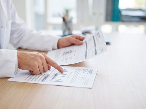 Close-Up of Doctor Hands Comparing Two Medical Reports on Desk in Bright Clinic with High Key Lighting and Soft Blurred Office Background