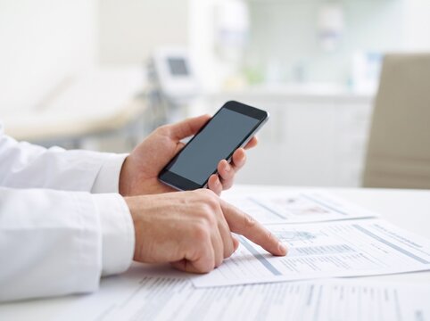 Close-Up of Doctor Using Smartphone While Reviewing Medical Document in Bright Clinic with Soft Blurred High Key Healthcare Background
