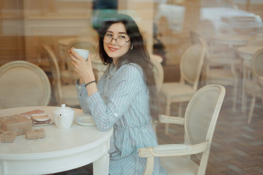 beautiful asian girl enjoying an hot tea in cafe while waiting for someone and having present box on a table, view through window glass