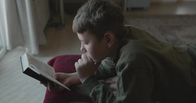 Caucasian Boy Kid Read Bible Book Lying on Bed in Bedroom. 4K 10-bit