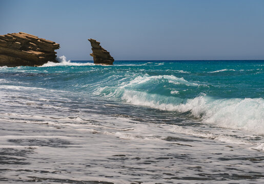 A landscape with waves of the blue Mediterranean Sea crashing onto a sandy beach