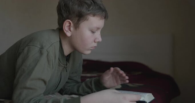 Caucasian Boy Kid Read Bible Book Lying on Bed in Bedroom. 4K 10-bit