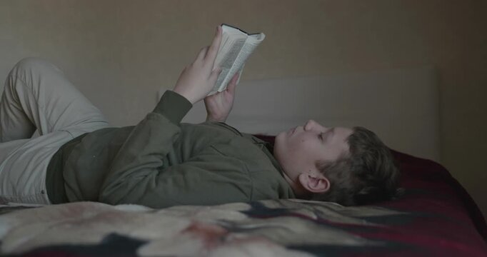 Caucasian Boy Kid Read Bible Book Lying on Bed in Bedroom. 4K 10-bit