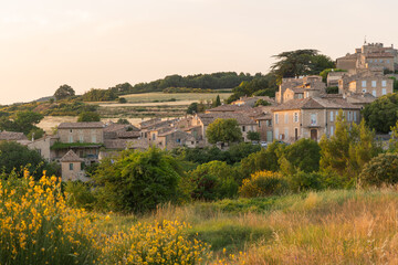 Obraz premium Golden evening light falls across the hillside village of Murs in the Vaucluse department of Provence, France, with wildflowers and dry grass in the foreground and stone houses