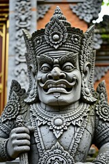 Obraz premium Ancient Balinese stone statue guard in Indonesian temple. Detail view of mythical creature sculpture with traditional ornaments at Hindu religious site. Travel destination with ornate craftsmanship