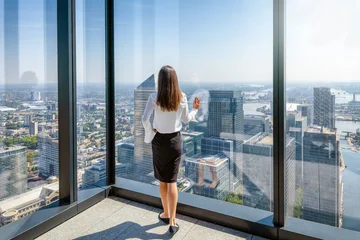 A business woman in corporate outfit looks at the skyline of the financial district Canary Wharf in London from her office window © moofushi