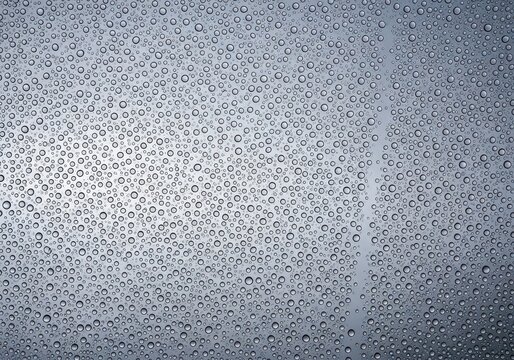 Clear glass surface covered in thousands of small water droplets reflecting a soft gray sky during a calm spring rainstorm in the evening, pane, trickle, raindrops
