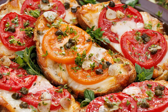 Grilled sourdough bread sandwiches, bruschettas with mozzarella and grana padano cheese, tomatoes, capers and garlic seasoned with aromatic herbs, close-up view