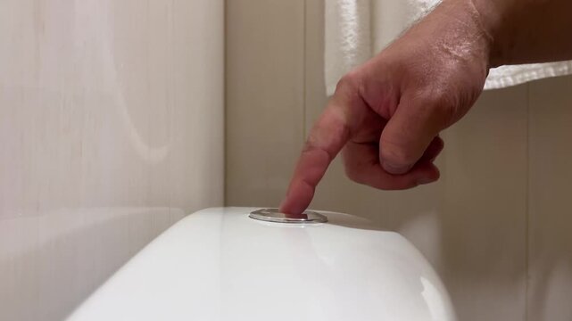 Horizontal 4K video close up. 60 fps. Male hand presses touch flush button on ceramic toilet cistern in public WC, home restroom, bath room. Concept of problems with diarrhea, urinary incontinence