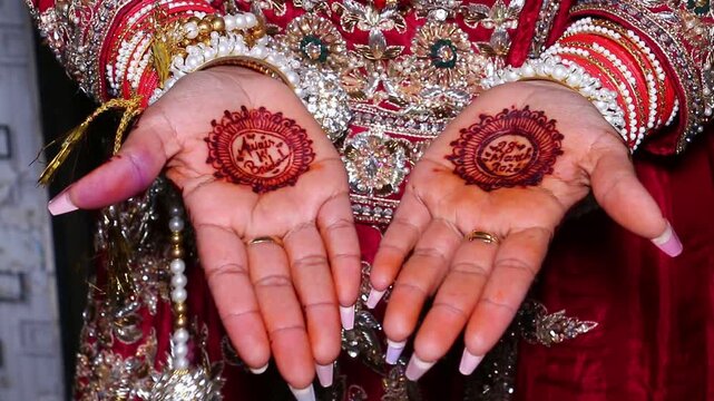Close up of hands displaying intricate mehndi henna designs and traditional jewelry on red fabric with patterns jewelry against red textured background