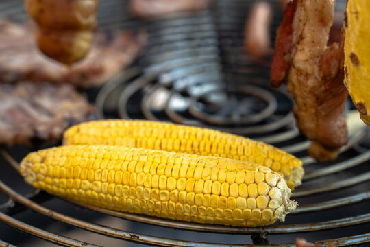 Fresh corn on the cob being grilled over hot coals, turning golden and slightly charred, representing smoky flavor, summer cooking, and outdoor barbecue food experience.