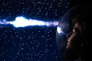 Conceptual side profile of a young boy looking at a bright galaxy and stars field through a futuristic glass helmet or window © Stefano Pessina