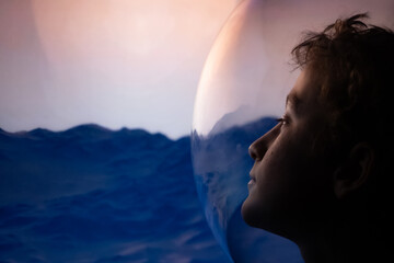 Conceptual profile portrait of a young boy astronaut in a glass helmet looking at a cinematic sunset over an alien planet landscape © Stefano Pessina