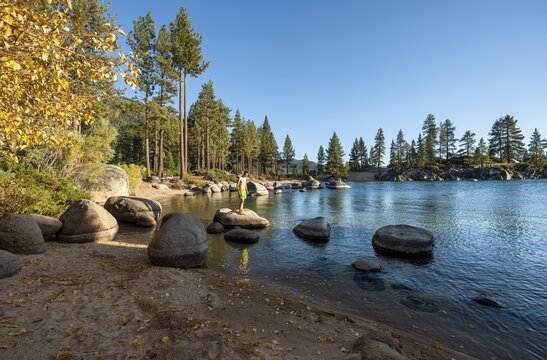 Young man in swimming trunks on round stones in the water, on sandy beach, bay at Lake Tahoe, Sand Harbor Beach, in autumn, Sand Harbor State Park, shore, California, USA