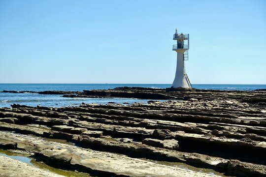 White Aoshima Lighthouse with fluted wave-cut rocks showing depth under blue sky