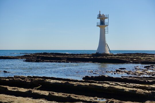 White Aoshima Lighthouse standing on fluted wave-cut rocks with textured foreground