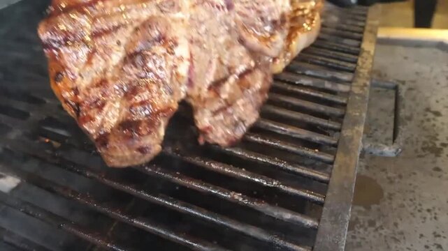 High-quality close-up footage of thick T-bone steaks cooking on a hot outdoor grill. The scene captures rising smoke, beautiful sear marks, and the sizzling texture of prime beef being prepared for a 