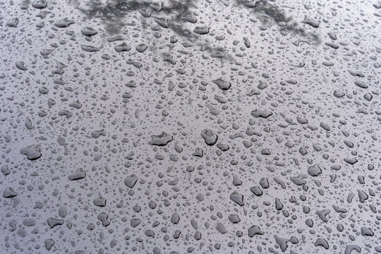 Close-up of a smooth reflective surface covered with numerous water droplets of varying sizes.
